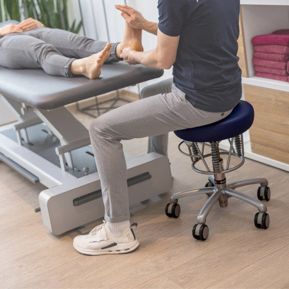 Ein blauer Foxter von Haider Bioswing im Einsatz als ergonomischer Drehhocker in einer Therapiesitzung einer Praxis