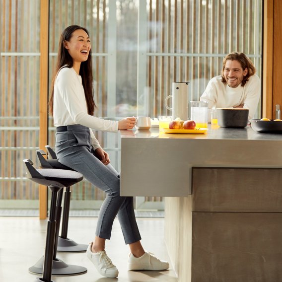 Settingfoto eines Aeris Muvman Stehhocker mit einer lachenden Frau drauf sitzend beim Fr&uuml;hst&uuml;ck
