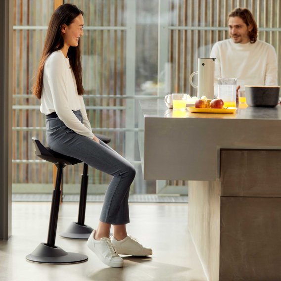 Settingfoto eines Aeris Muvman Stehhocker mit einer Frau drauf sitzend beim Fr&uuml;hst&uuml;ck