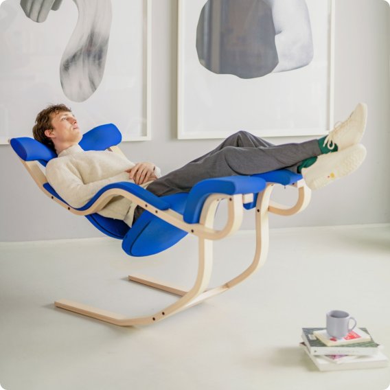 Junger Mann auf einem Varier Gravity mit blauem Bezug und eschenfarbenen Gestell in der Liegeposition.
