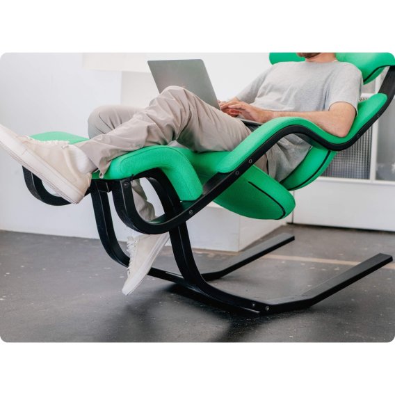 Varier Gravity mit schwarzem Gestell und gruenem Bezug mit einem Mann in der Leseposition am Laptop arbeitend.