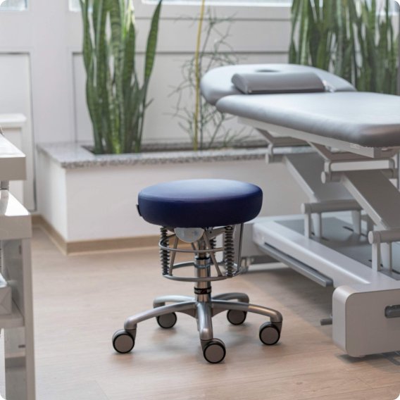 Freistehender Bioswing Foxter Praxishocker vor einer Patientenliege.